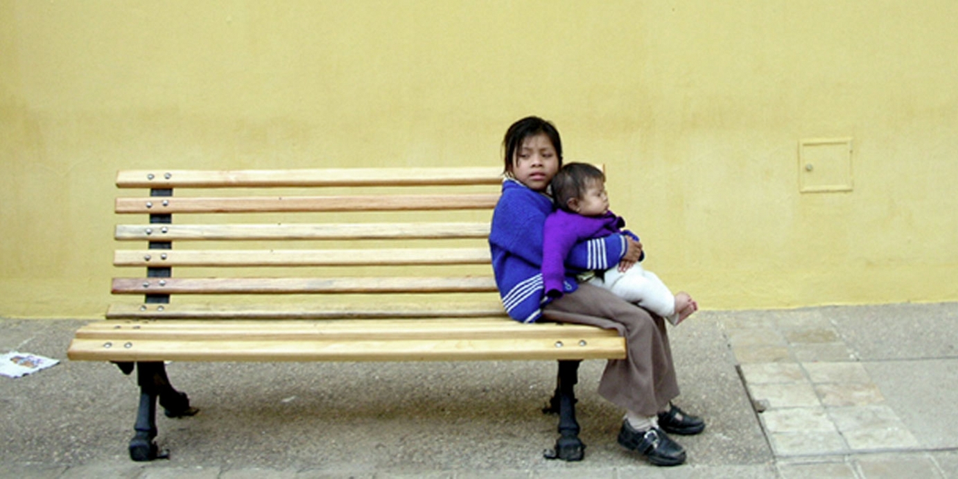 Child sitting on bench holding baby