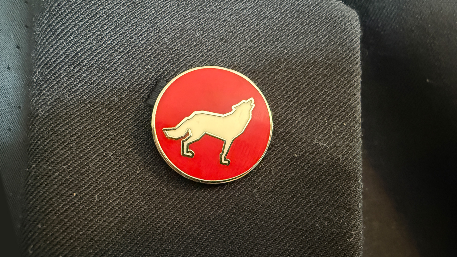 A circle label pin with a red background and a white wolf illustration.