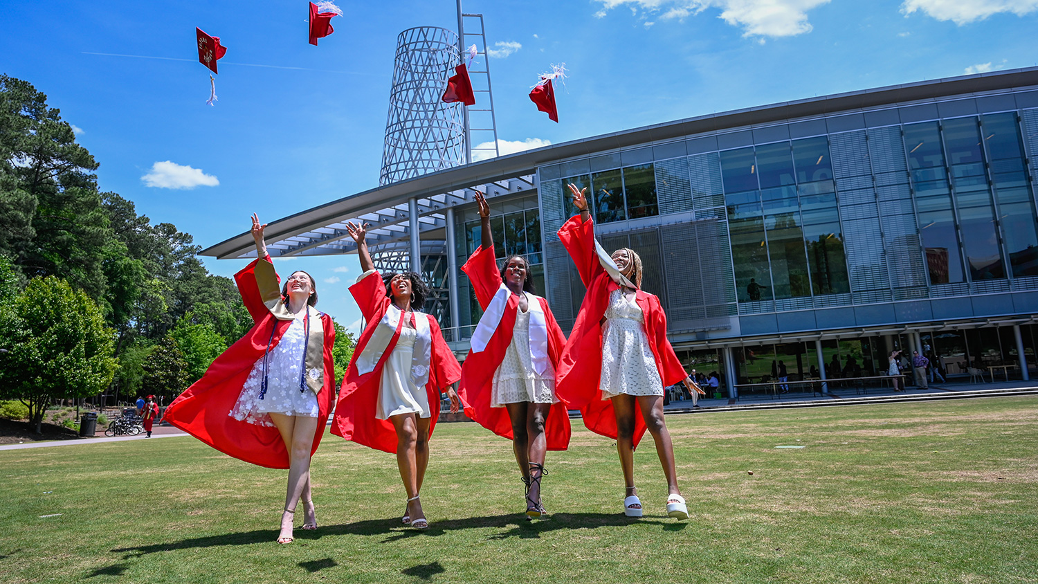 Four women in red robes throw their graduation caps in the air.