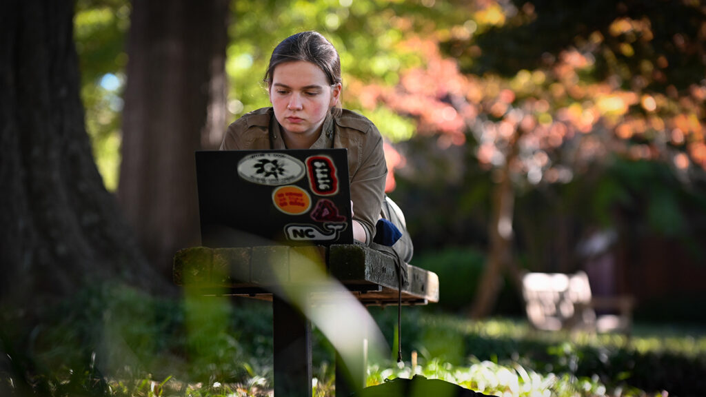 A student works on a laptop covered in stickers.
