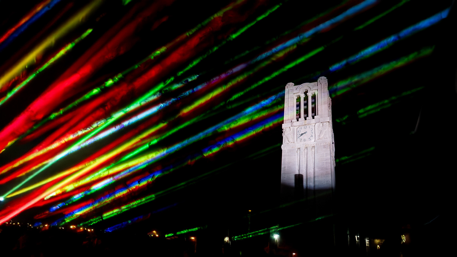 NC State's Memorial Belltower at night, surrounded by colorful lights.